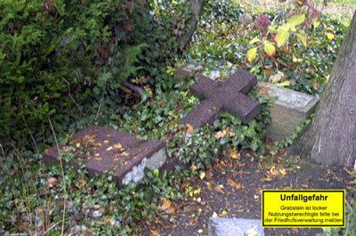 Sichere Grabsteine durch fachgerechte Reparatur – Steinmetzbetrieb Tauchert Umgefallener, bemooster Grabstein auf einem Friedhof mit Warnschild "Unfallgefahr"; Reparatur durch Steinmetzbetrieb Tauchert.